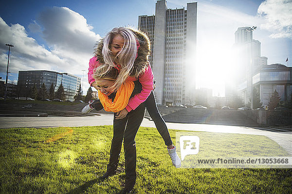 Female friends playing on grassy field against cityscape