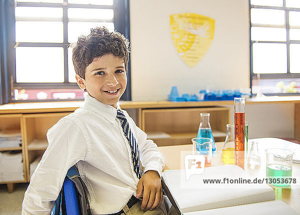 Porträt eines glücklichen Schuljungen  der im Labor am Tisch sitzt