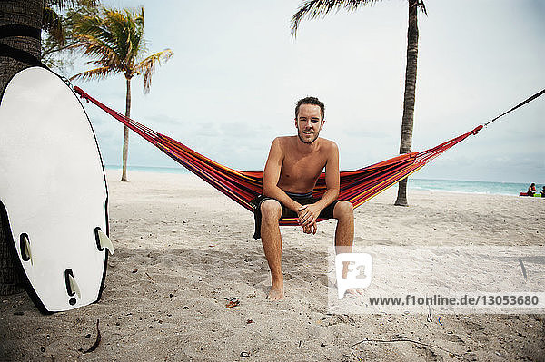 Porträt eines Mannes  der auf einer Hängematte am Strand gegen den Himmel sitzt