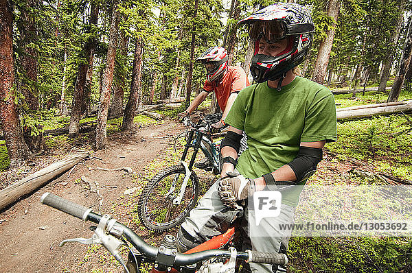 Mountain bikers looking away while sitting on bicycles in forest