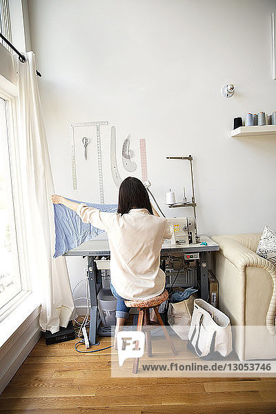 Rückansicht eines Modedesigners  der Stoff hält  während er auf einer Nähmaschine sitzt