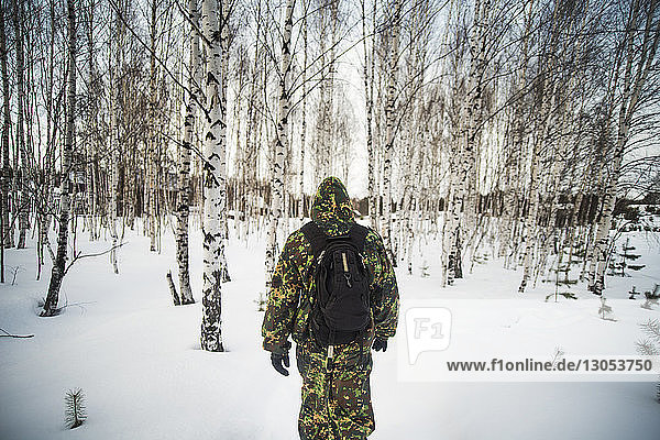 Rückansicht eines jungen Mannes  der auf einem schneebedeckten Feld im Wald steht