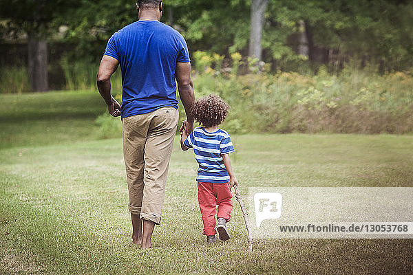 Father and son holding hands while walking on grassy field