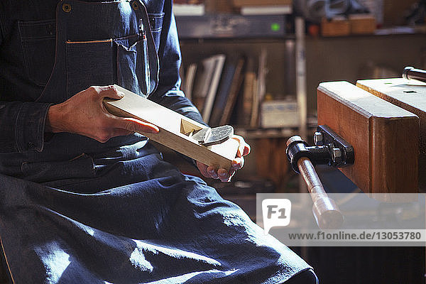 Mittelteil eines Tischlers  der ein Holzhobel hält  während er in der Werkstatt sitzt