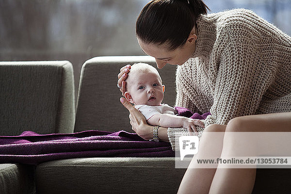 Mother holding cute baby girl on sofa at home