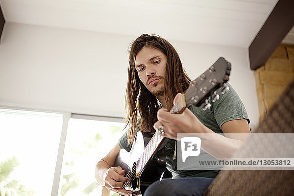Niedriger Blickwinkel auf einen Mann  der zu Hause auf dem Sofa sitzt und Gitarre spielt