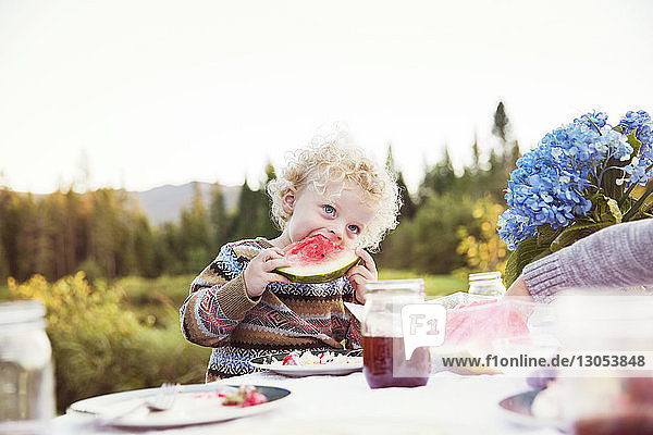 Boy eating watermelon on picnic table against clear sky