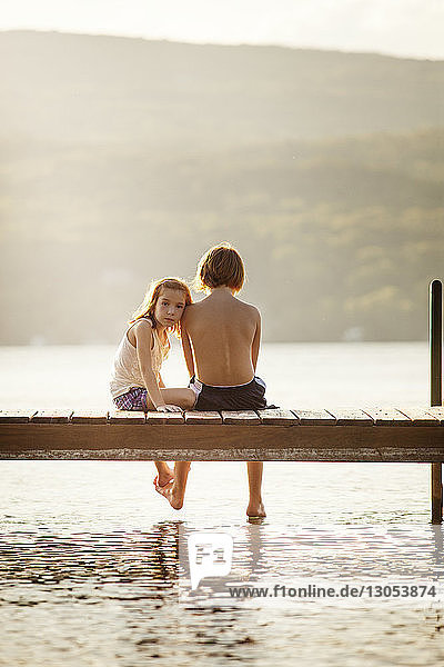 Porträt der Schwester  die mit dem Bruder auf dem Steg über dem See sitzt