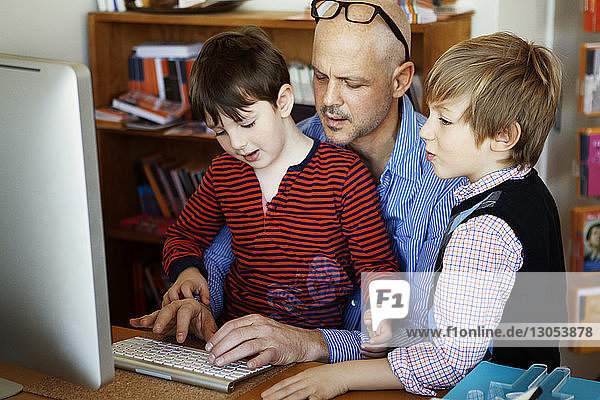 Vater und Söhne nutzen Desktop-Computer zu Hause