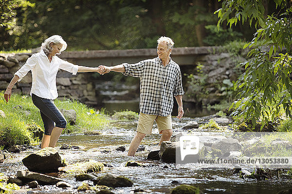 Älterer Mann hilft Frau beim Überqueren des Flusses