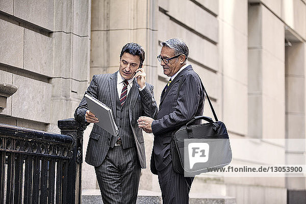 Businessmen looking at file while standing at city street