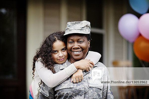 Portrait of happy daughter embracing soldier against house