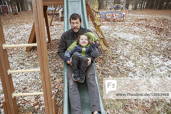 Father and son sliding on slide at park