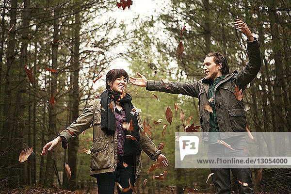 Playful couple throwing leaves while standing in forest
