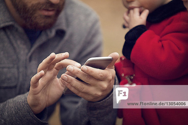 Mittelsektion eines Vaters mit einem kleinen Mädchen  das ein Smartphone im Park benutzt