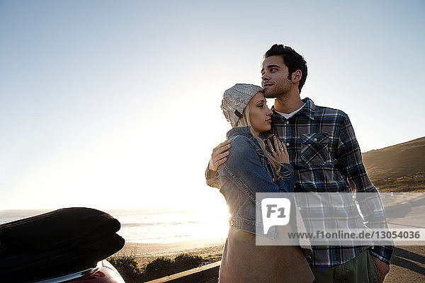 Junges Paar umarmt sich an einem sonnigen Tag gegen den Himmel
