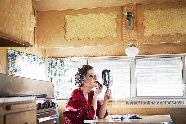 Seitenansicht einer Frau  die Lippenstift aufträgt  während sie im Wohnmobil am Tisch sitzt