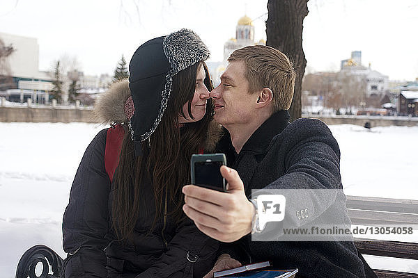 Romantic man taking selfie with girlfriend sitting on bench in park
