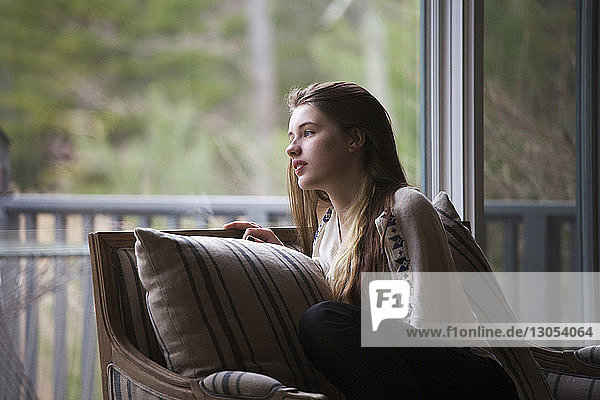 Teenagerin schaut weg  während sie zu Hause auf dem Sofa sitzt