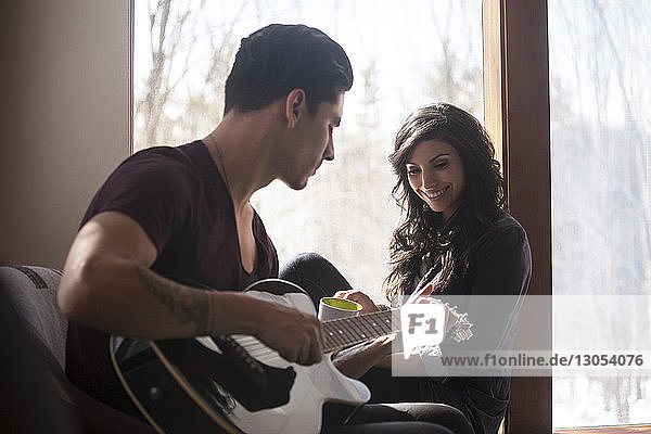 Man playing guitar while woman sitting on window sill