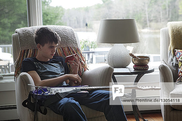 Junge sieht Handy an  während er zu Hause auf einem Sessel sitzt