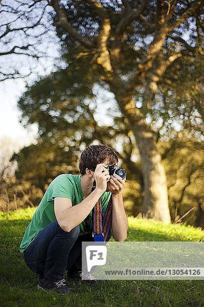 Man photographing while crouching on grassy field