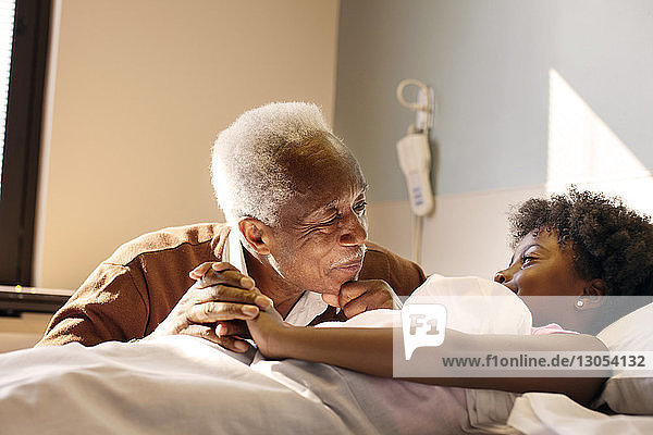 Grandfather looking at girl lying on bed in hospital