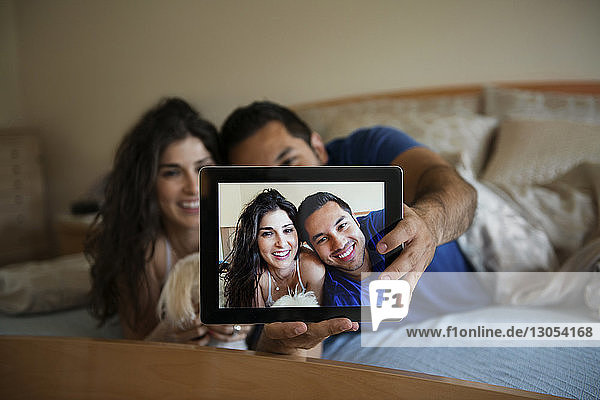 Happy couple taking selfie through tablet computer while relaxing on bed