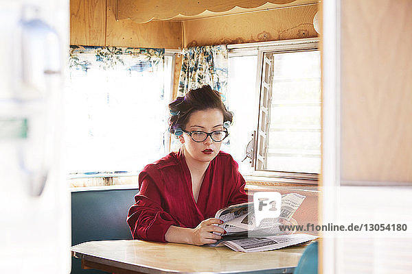 Frau liest Zeitung  während sie im Wohnmobil am Tisch sitzt
