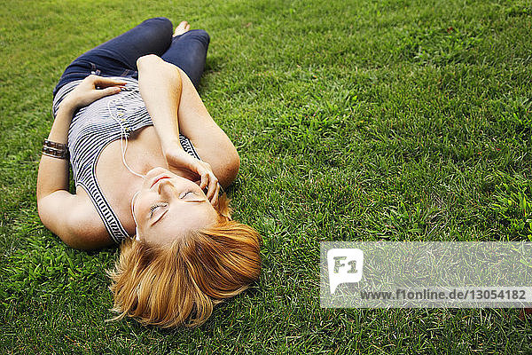 Frau hört Musik  während sie auf einem Grasfeld im Park liegt