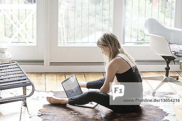 Frau benutzt Laptop  während sie zu Hause auf dem Boden sitzt