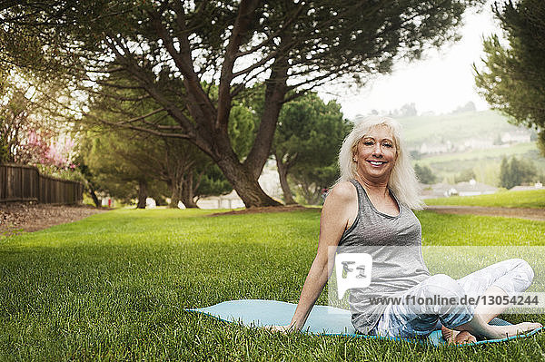 Porträt einer glücklichen Frau  die auf einer Fitnessmatte im Park sitzt