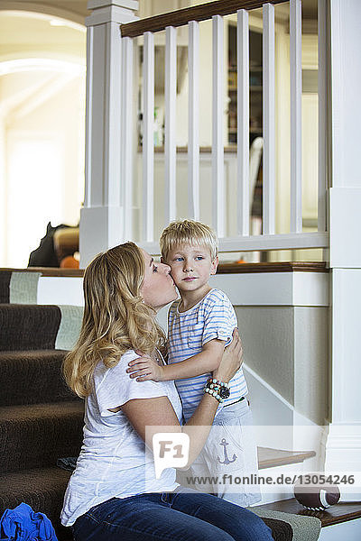 Mutter küsst Sohn auf Treppenstufen zu Hause