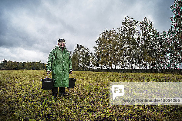Portrait of male farm worker standing on field against cloudy sky