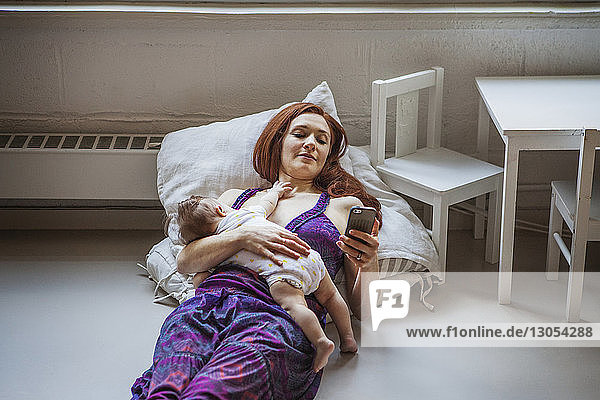 High angle view of mother with baby girl using mobile phone while lying on floor at home