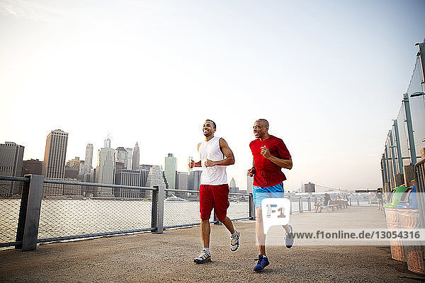 Glücklicher Mann und Vater joggen auf der Promenade am East River in der Stadt bei klarem Himmel