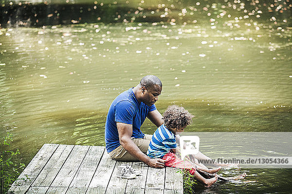 Vater und Sohn sitzen mit den Füßen auf einem Steg im See