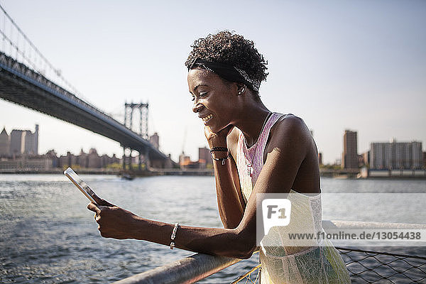 Happy woman using tablet computer by river with Manhattan Bridge in background