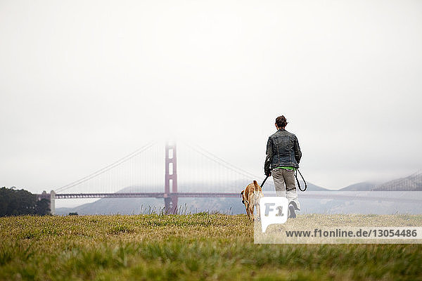 Rear view of woman and dog walking on grassy field at Golden Gate Park