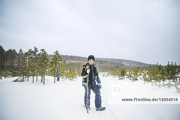 Portrait of boy holding stick while standing on snow covered field against clear sky