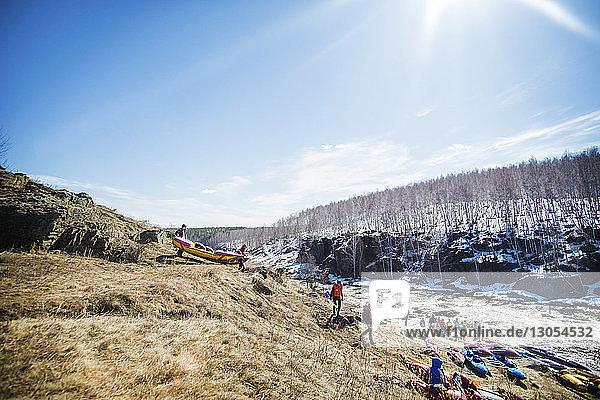 Friends carrying boats on hill by river during sunny day