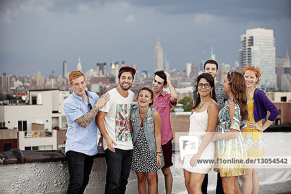 Happy friends standing on building terrace against city