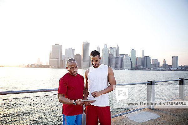 Man and father using tablet computer while standing by East River in city against clear sky