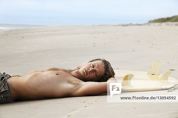 Portrait of man with surfboard lying on sand