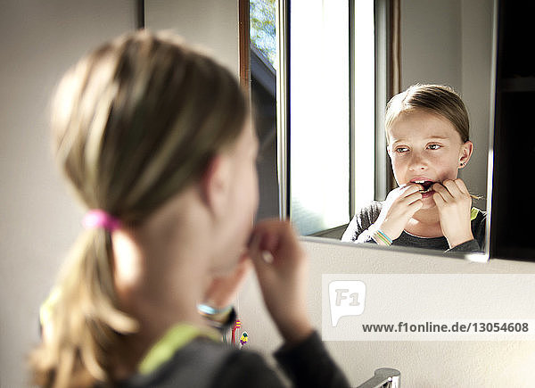 Girl flossing teeth in bathroom seen through mirror