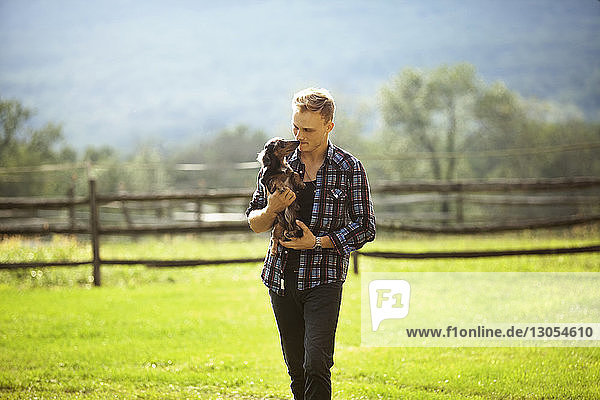 Man carrying dog while walking on grassy field in farm