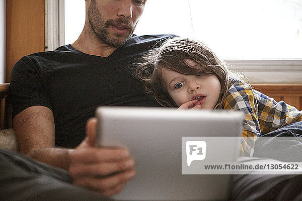 Vater und Sohn benutzen Tablet-Computer  während sie sich zu Hause im Bett entspannen