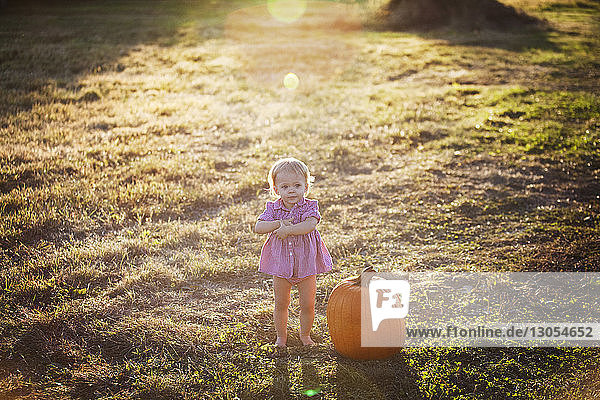 Süßes Baby-Mädchen steht neben Kürbis auf Grasfeld