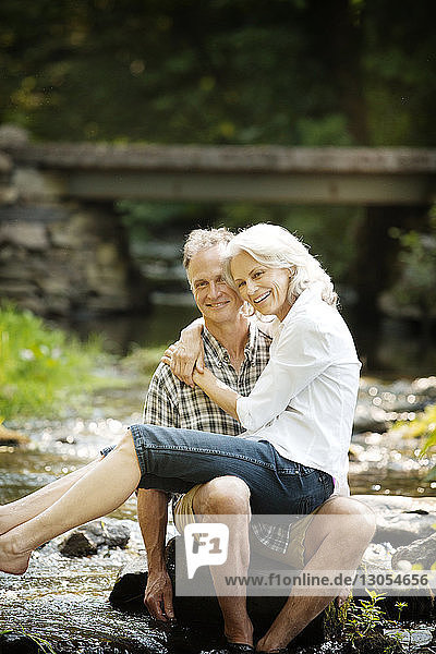 Portrait of happy senior woman sitting on man's lap in stream
