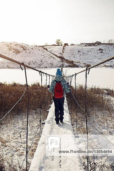Rear view of woman with backpack walking on snow covered footbridge